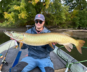 Man in boat holding large muskellunge toward camera