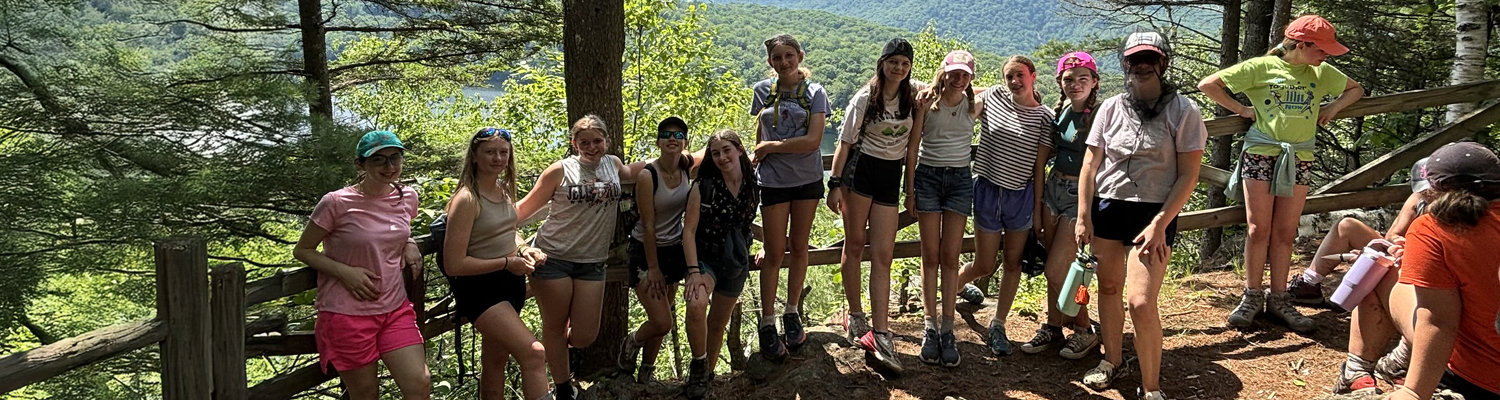 Advanced Week Girls group of about 10 young teens lined up at a scenic viewpoint at camp.